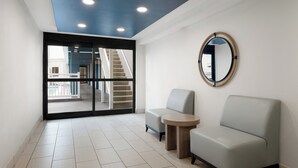 Un espace d’attente moderne avec un canapé de couleur claire, une petite table ronde et un miroir au mur.