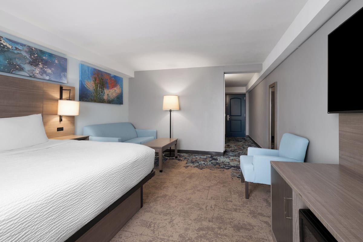 A hotel room with a bed, a desk, a chair, a TV, and artwork on the walls.