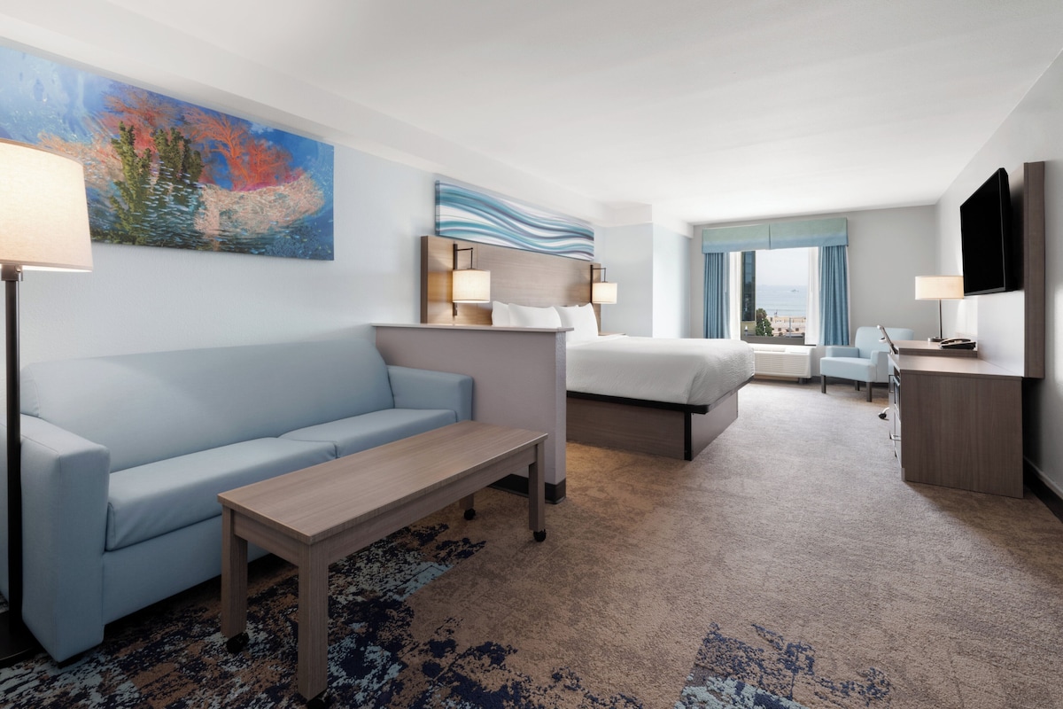Una habitación de hotel con un sofá azul claro, una mesa de madera, una cama con cabecera, un escritorio con una silla y un televisor en la pared.