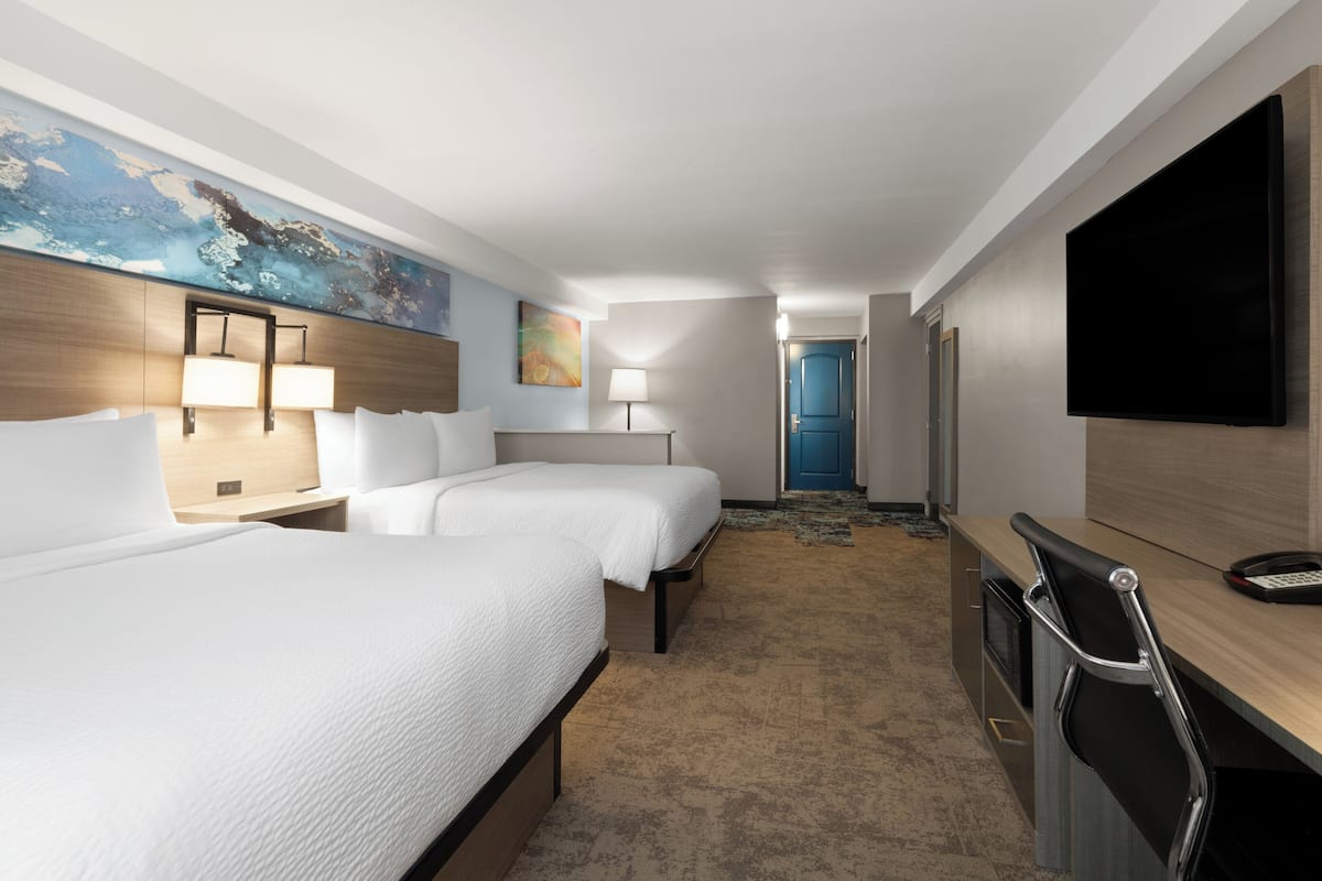 A hotel room with two beds, a desk with a chair, a flat-screen TV, and a large painting on the wall.
