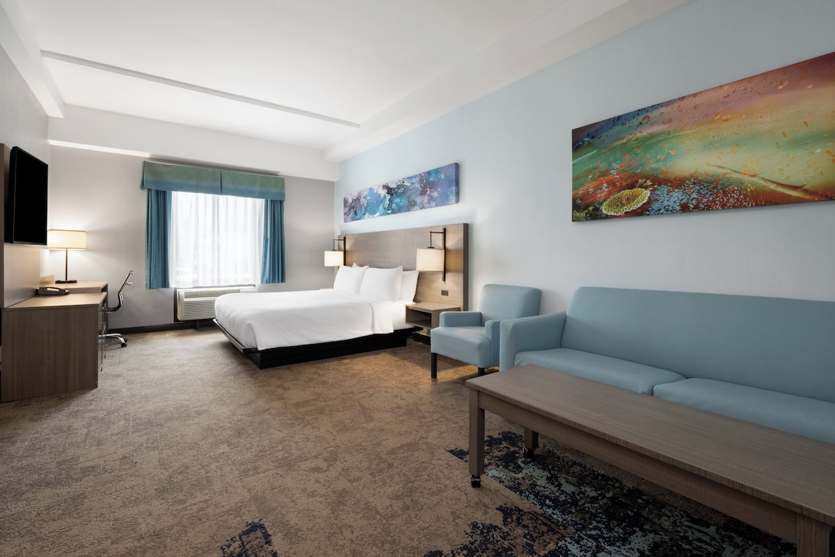 A hotel room with a bed, a sofa, a desk, a lamp, and a painting on the wall.