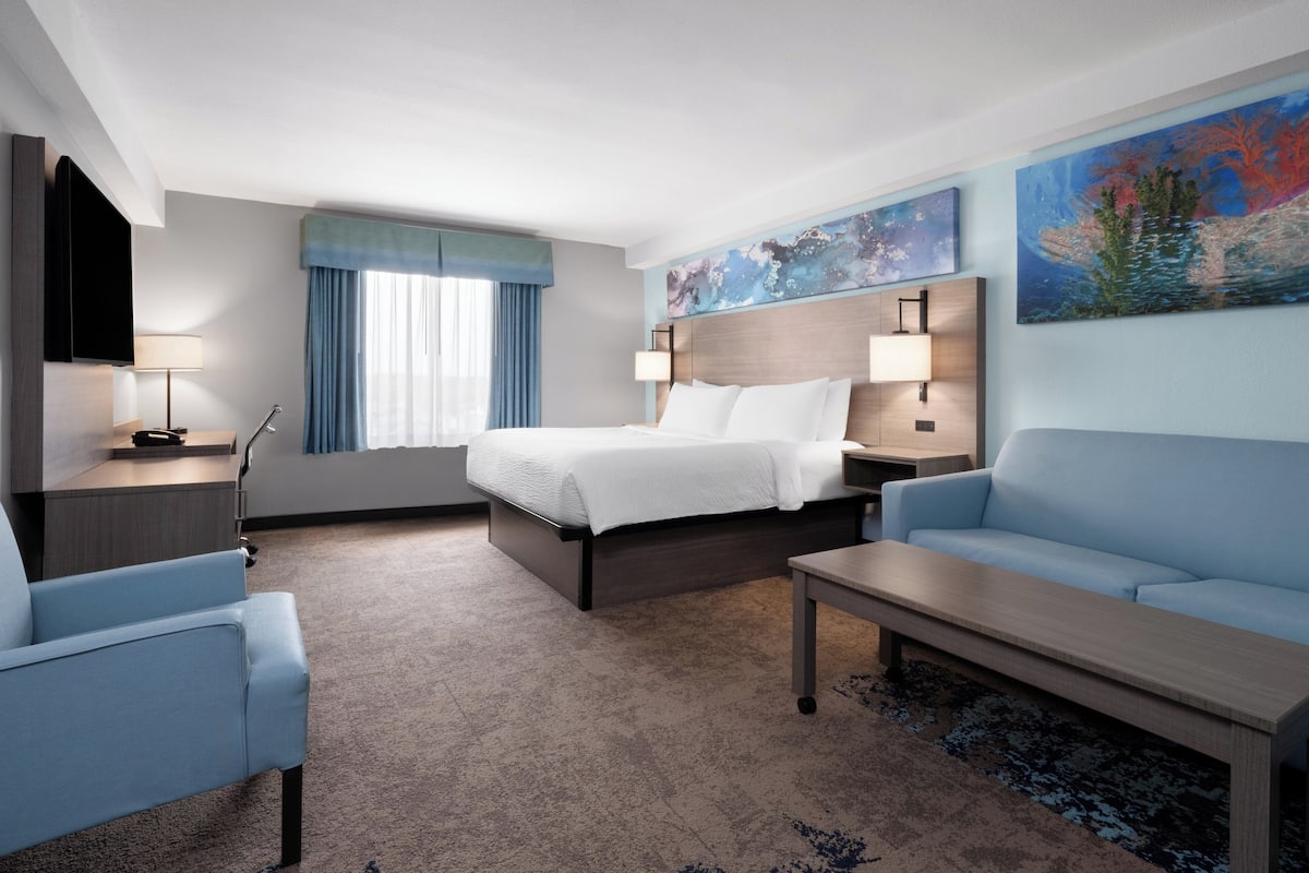 A hotel room with a bed, a sofa, a desk, a TV, and artwork on the walls.