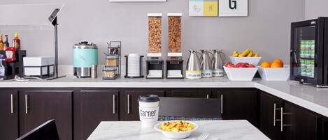 Une cuisine moderne dotée d’un plan de travail en marbre, d’une machine à café, d’une bouilloire, d’un saladier rempli de fruits et d’un réfrigérateur.