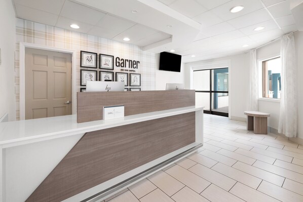 A hotel reception desk with a modern design, framed artwork on the wall, and a flat-screen TV above it.