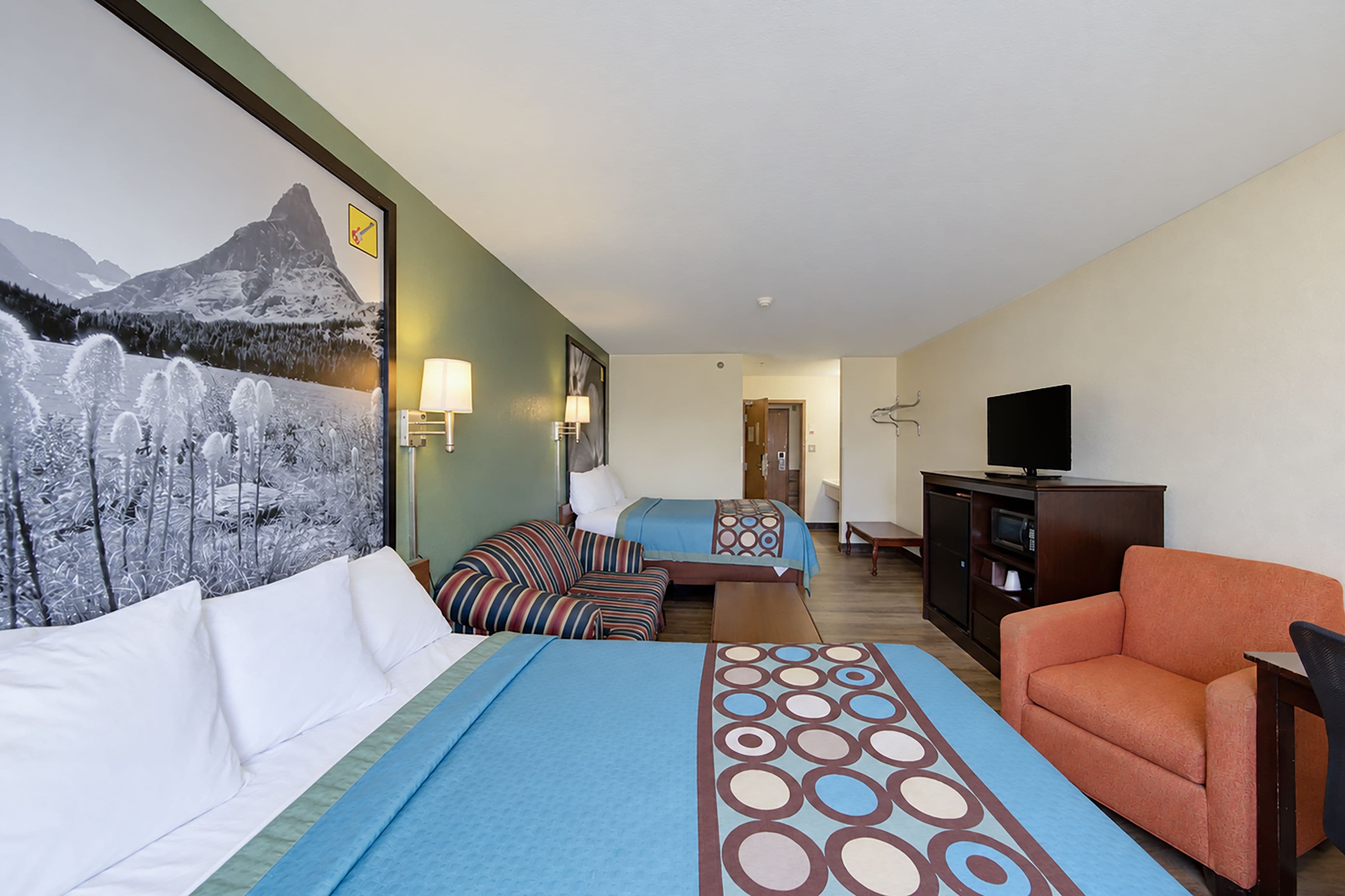 A hotel room with two beds, a television, a desk, and a painting of a mountain landscape.