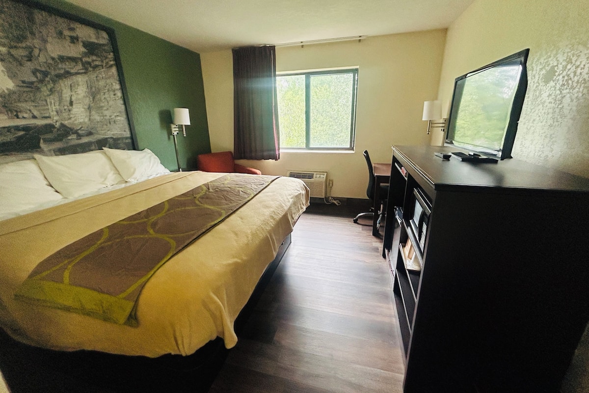 A hotel room with a bed, a desk, a television, a chair, and a window.