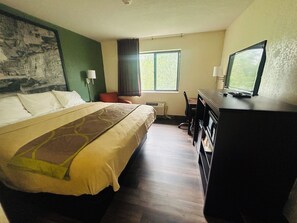 A hotel room with a bed, a desk, a television, a chair, and a window.