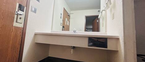 A bathroom with a wooden door, a mirror, a sink, and a trash bin.