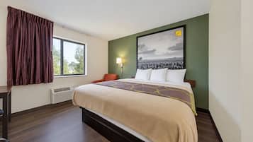 Une chambre d’hôtel avec un lit, une fenêtre avec des rideaux, une lampe fixée au mur et un grand tableau encadré.