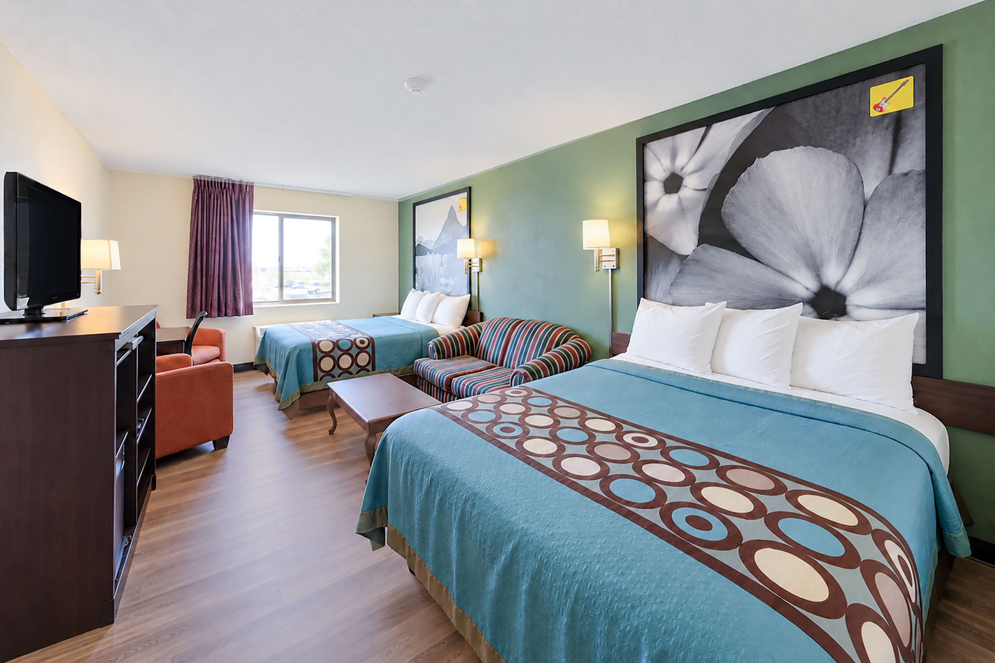 A hotel room with two beds, a desk, a television, and a large floral artwork on the wall.