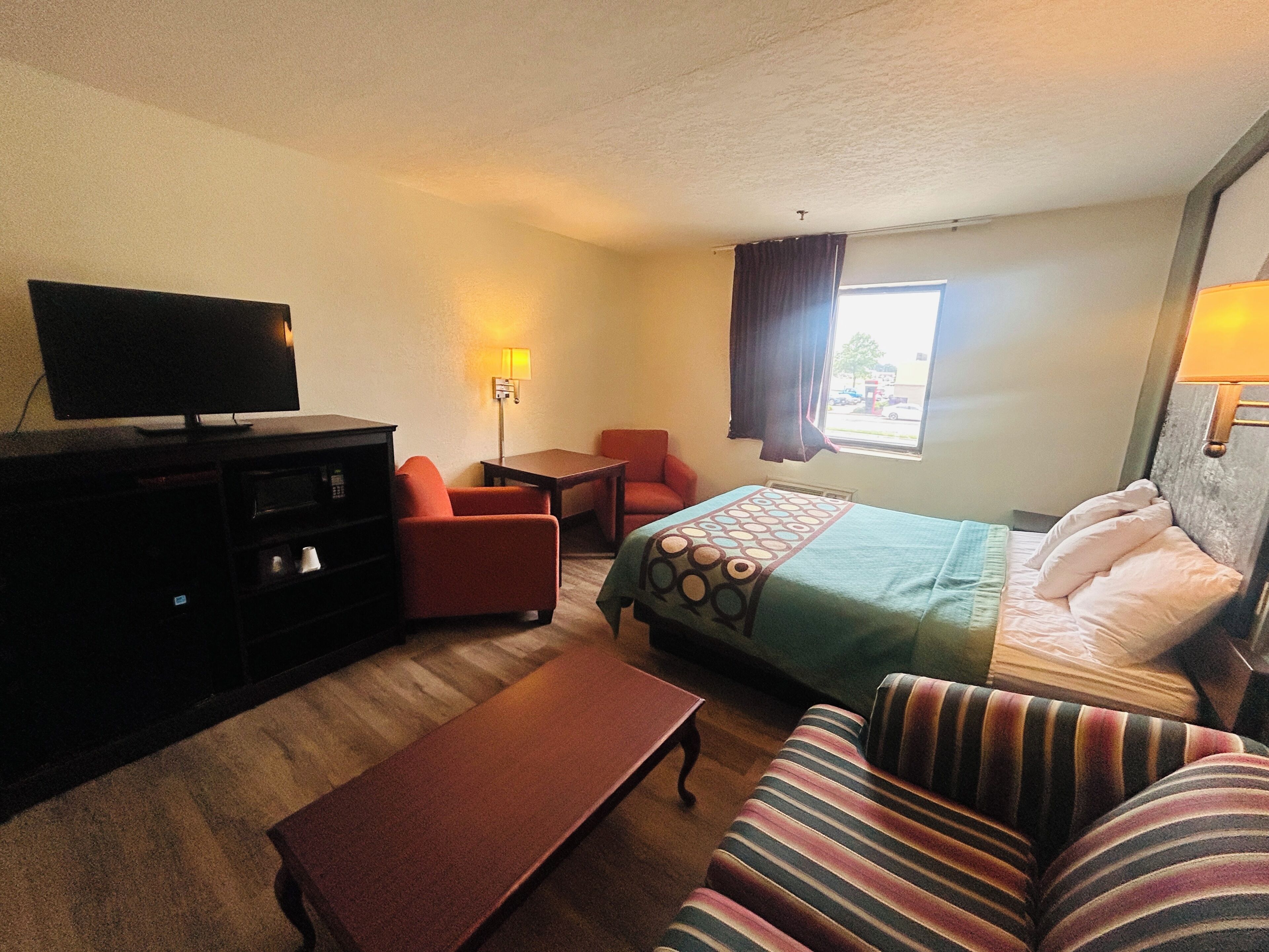 Una habitación de hotel con cama, sofá, televisor, escritorio y ventana con cortinas.