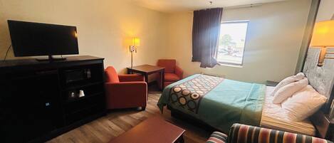 Una habitación de hotel con cama, sofá, televisor, escritorio y ventana con cortinas.