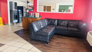 A living room with a black leather sectional sofa, a wooden cabinet, and a red wall.