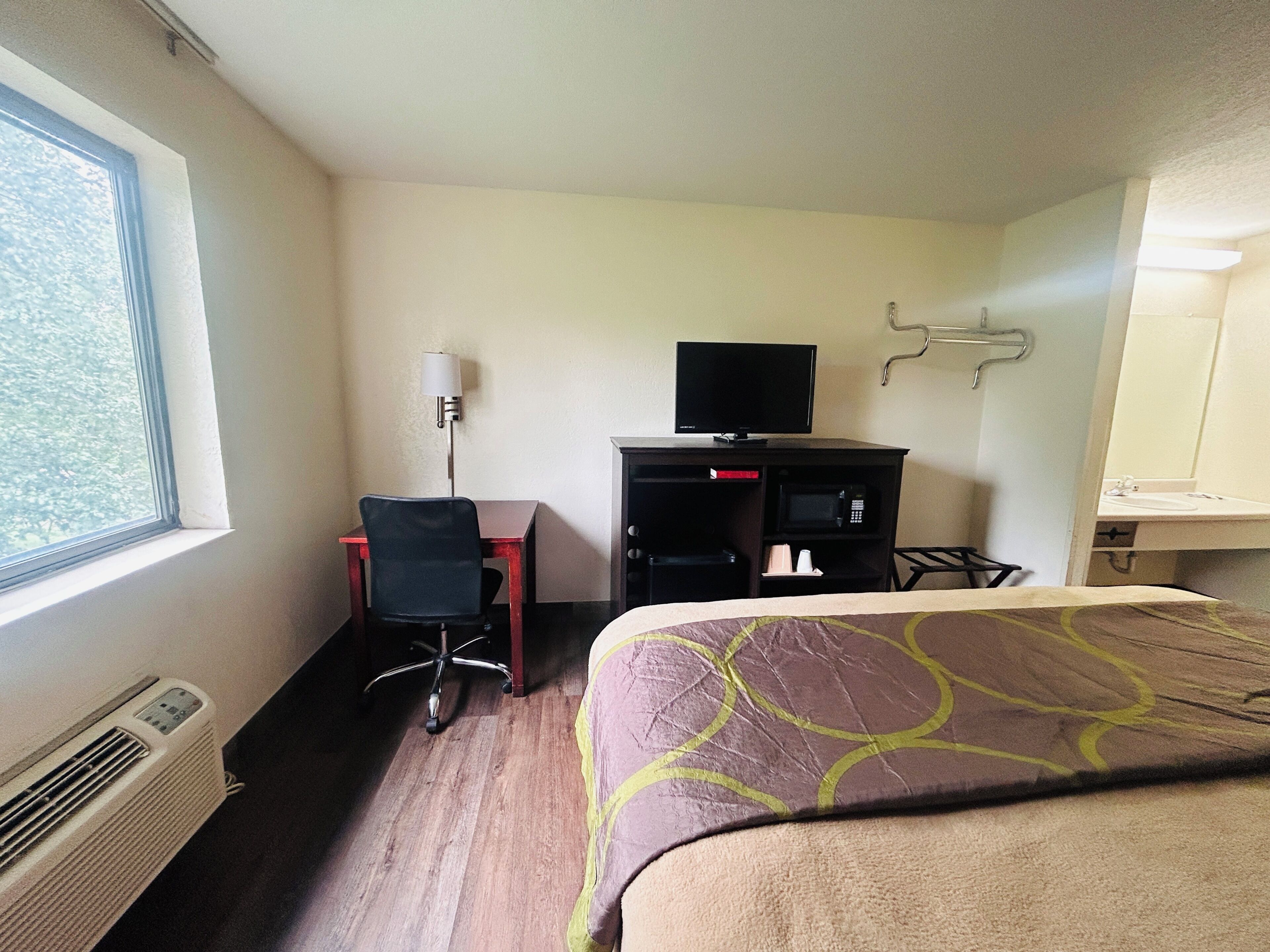 A hotel room with a bed, a desk with a chair, a TV, a microwave, and a window.