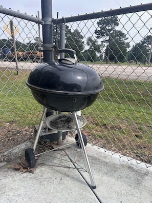 A portable barbecue grill with a lid, positioned on a concrete surface, surrounded by a chain-link fence.
