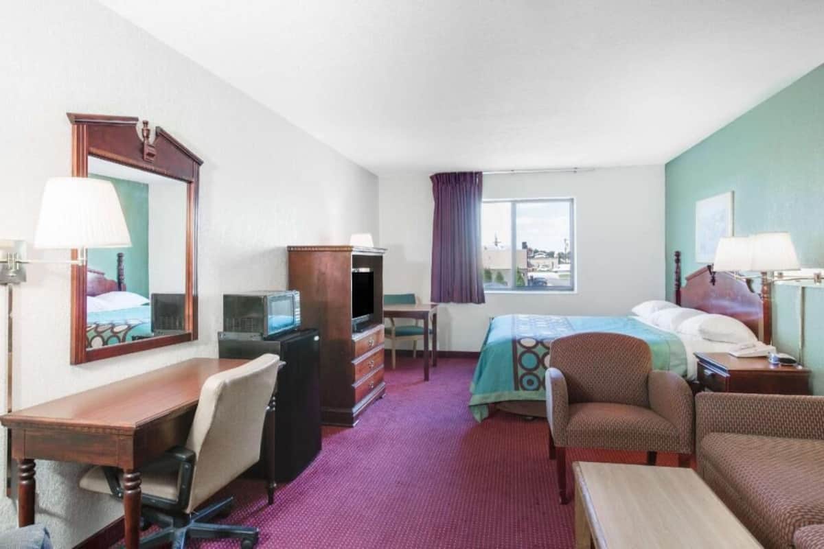 A hotel room with a bed, desk, chair, television, dresser, and a window with a view.
