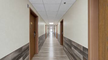 A long, narrow hotel corridor with doors on both sides, a tiled floor, and a ceiling with recessed lighting.