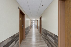 A long, narrow hotel corridor with doors on both sides, a tiled floor, and a ceiling with recessed lighting.