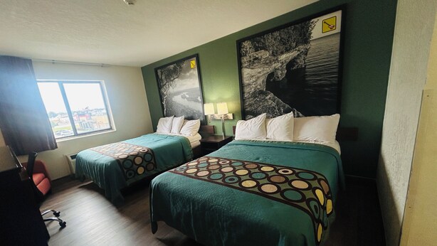 A hotel room with two beds, a desk, a chair, a window with a view, and a painting on the wall.