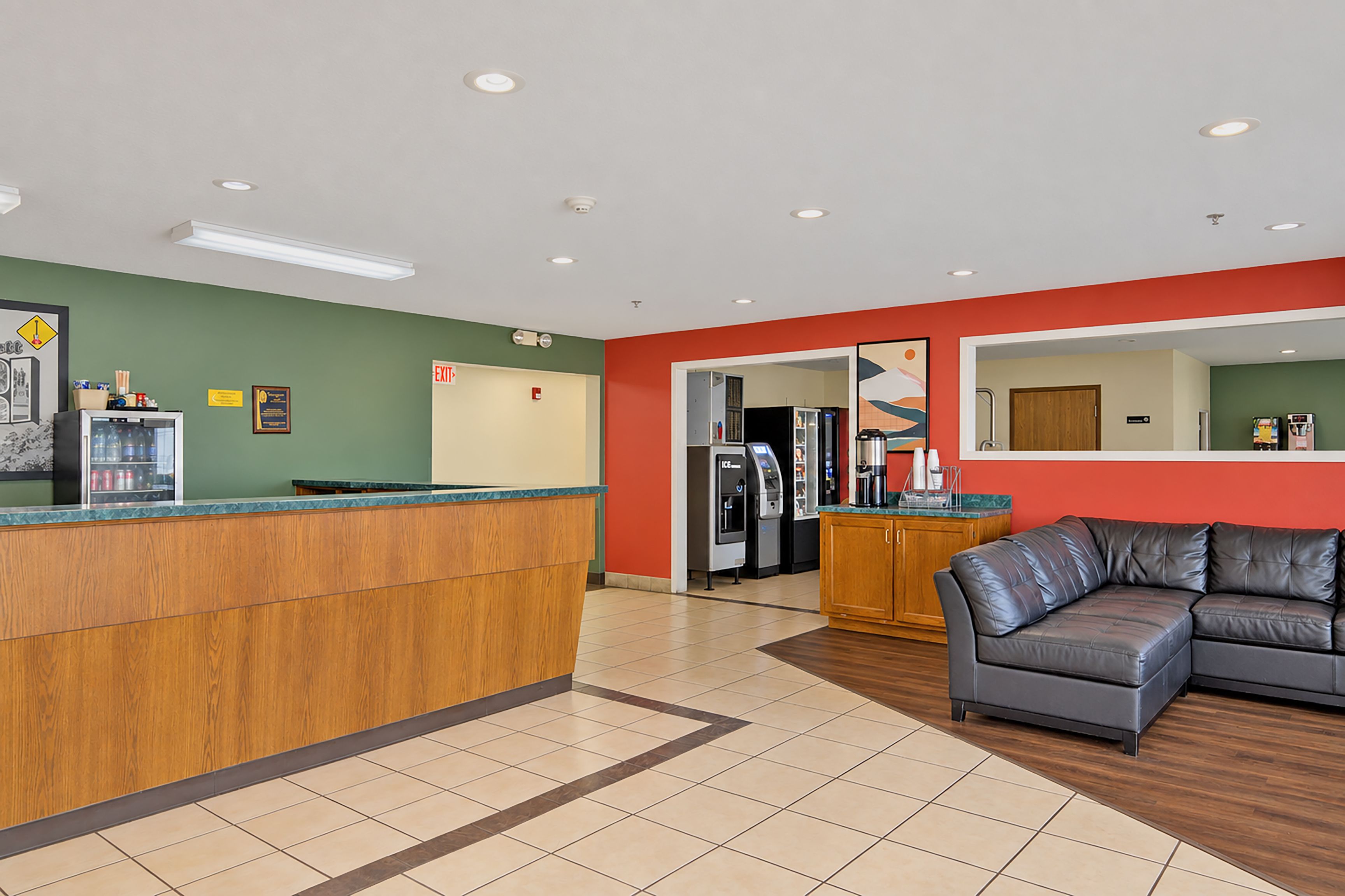 A reception area with a wooden counter, a refrigerator, a coffee machine, and a seating area with a leather couch.
