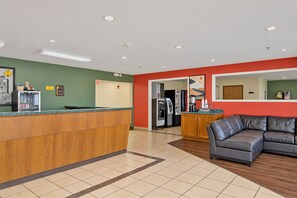 A reception area with a wooden counter, a refrigerator, a coffee machine, and a seating area with a leather couch.