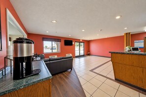 A hotel lobby with a reception desk, a coffee machine, a sofa, and a large window with blinds. - Rockwood Inn Kennett I 55 Near Blytheville (Kennett)