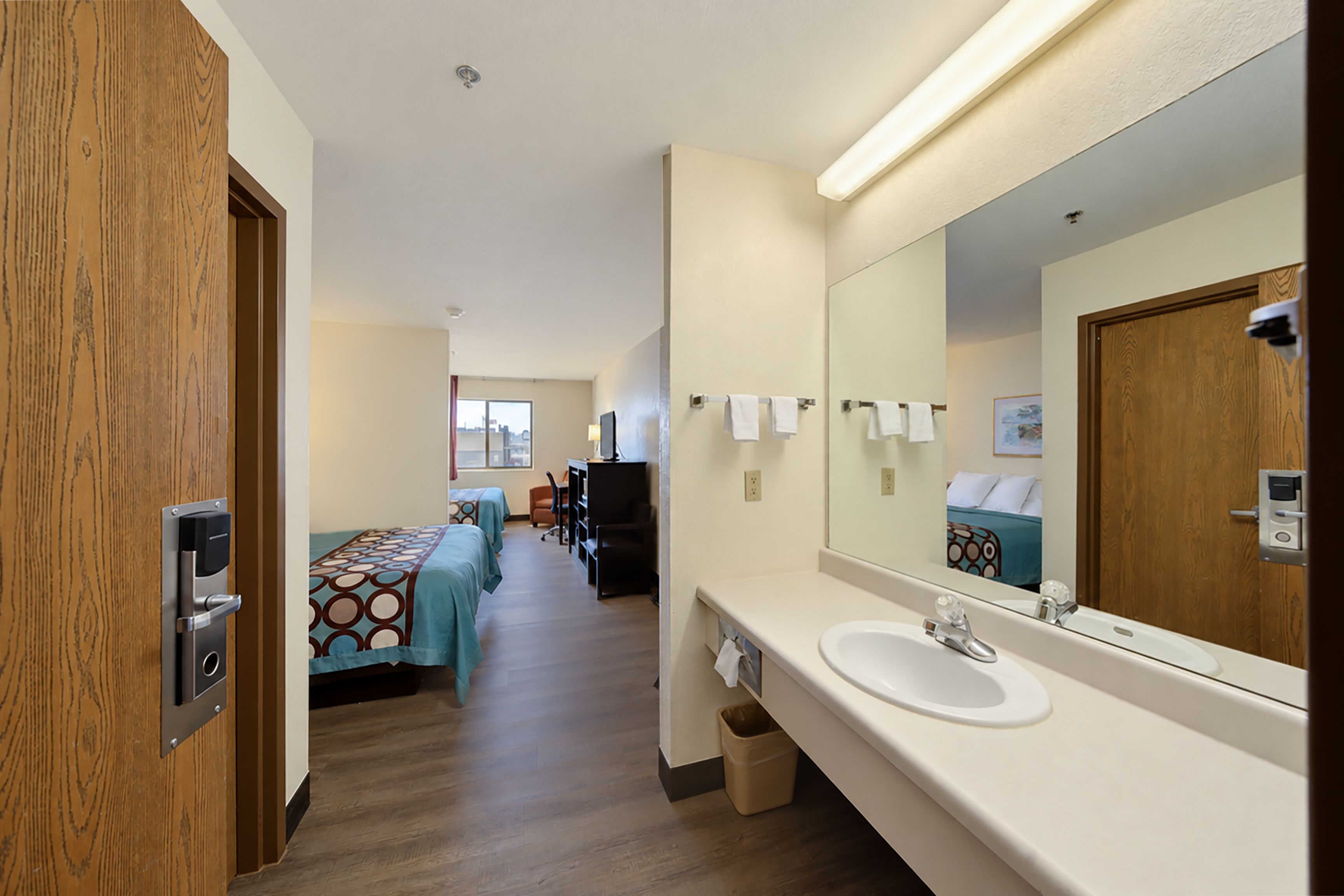 A hotel room with a large mirror, a sink, and a bed with patterned bedding.