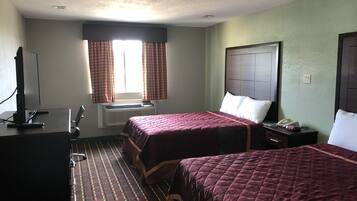 A hotel room with two beds, a TV, a desk, and a window with curtains.