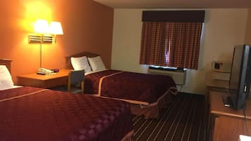 A hotel room with two beds, a desk, a chair, a lamp, a television, and a window with curtains.