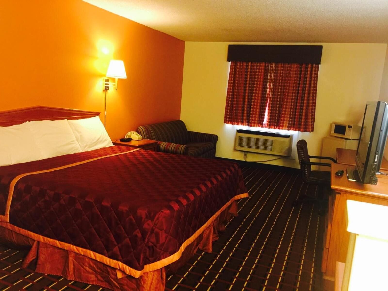 A hotel room with a large bed, a sofa, a desk with a computer, and a window with curtains.