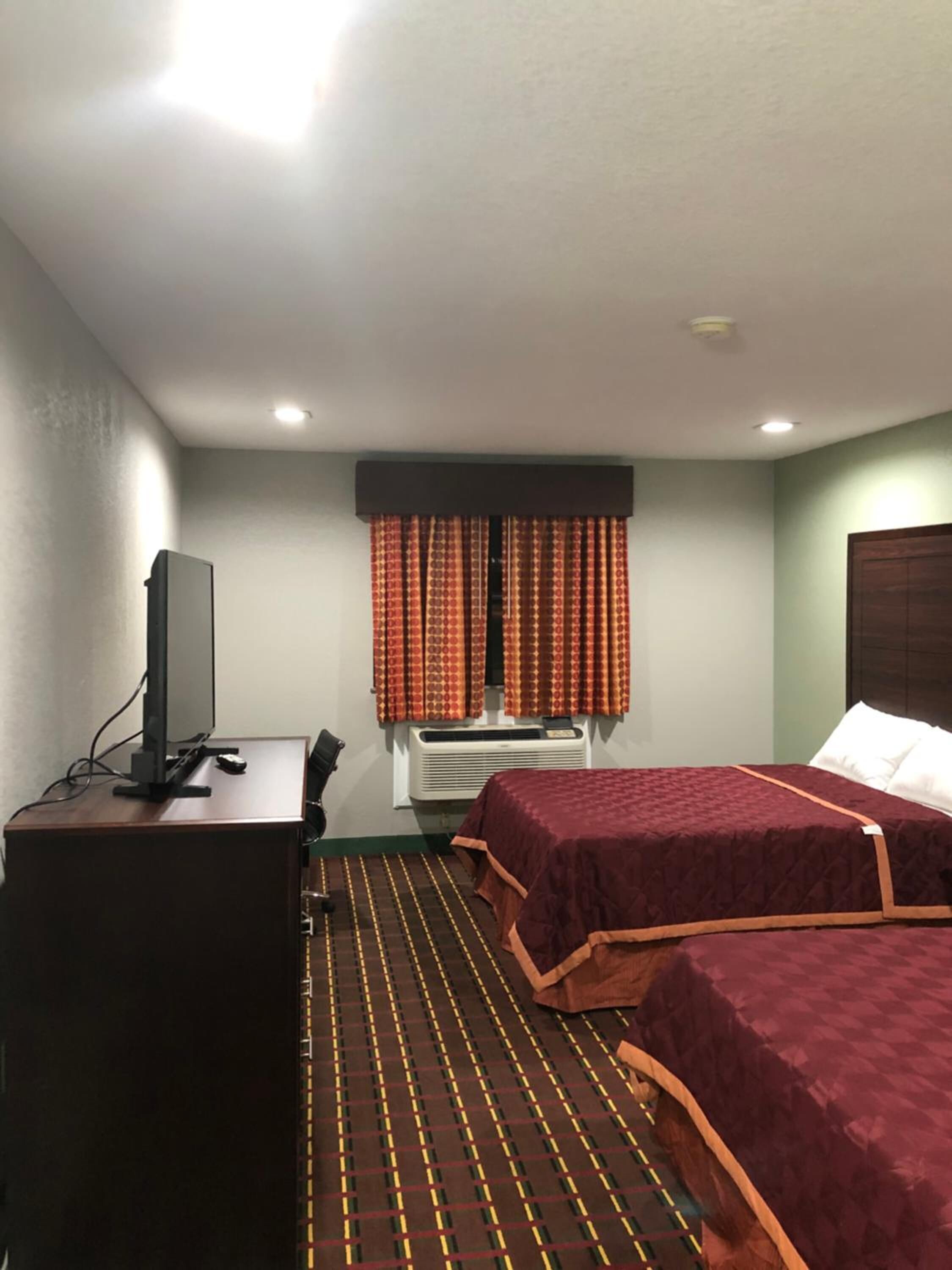 Habitación de hotel con dos camas, un escritorio con televisor y una ventana con cortinas.