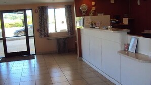 A reception area with a tiled floor, a counter with a framed picture, and a window with curtains. - Texas Inn & Suites (Lufkin)
