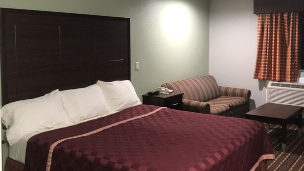 A hotel room with a large bed, a small sofa, a desk, and a window with curtains. - Texas Inn & Suites (Lufkin)