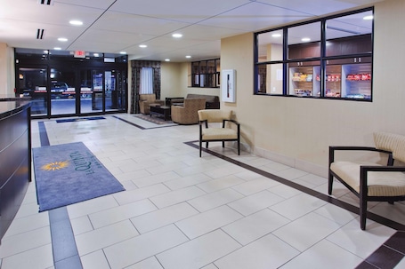 A hotel lobby with a reception desk, seating area, and a view of the street through large windows.