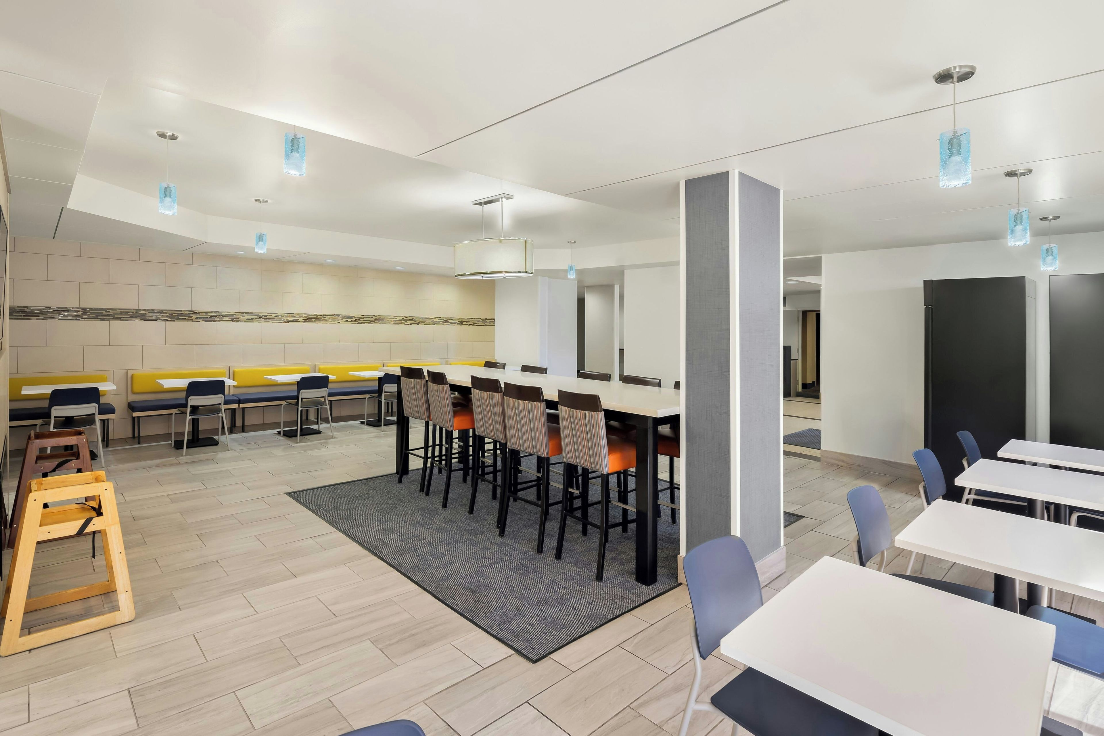 A modern dining area with high tables and chairs, a central seating area with benches, and pendant lighting.