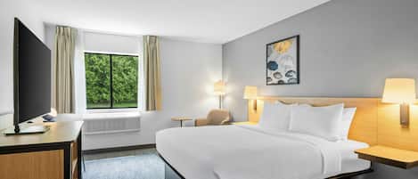 Habitación de hotel con cama, lámparas de noche, escritorio con computadora, ventana con cortinas y un cuadro en la pared.