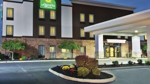 Um hotel La Quinta Inn & Suites com fachada de tijolos, várias janelas e uma área de jardim bem cuidada com diversas plantas e flores.