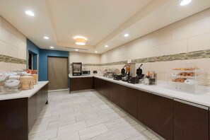 A modern kitchen area with a long counter, various appliances, and a display case with pastries. - La Quinta Inn & Suites by Wyndham Columbus - Grove City (Grove City)