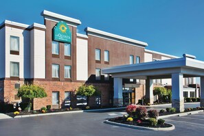 A La Quinta Inn & Suites building with a brick facade, a clear blue sky, and a landscaped entrance area. - La Quinta Inn & Suites by Wyndham Columbus - Grove City (Grove City)