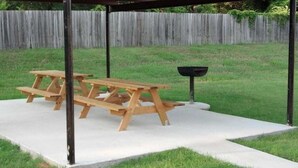 A wooden picnic table under a metal pergola in a grassy backyard with a wooden fence in the background. - Majestic Inn (Longview)