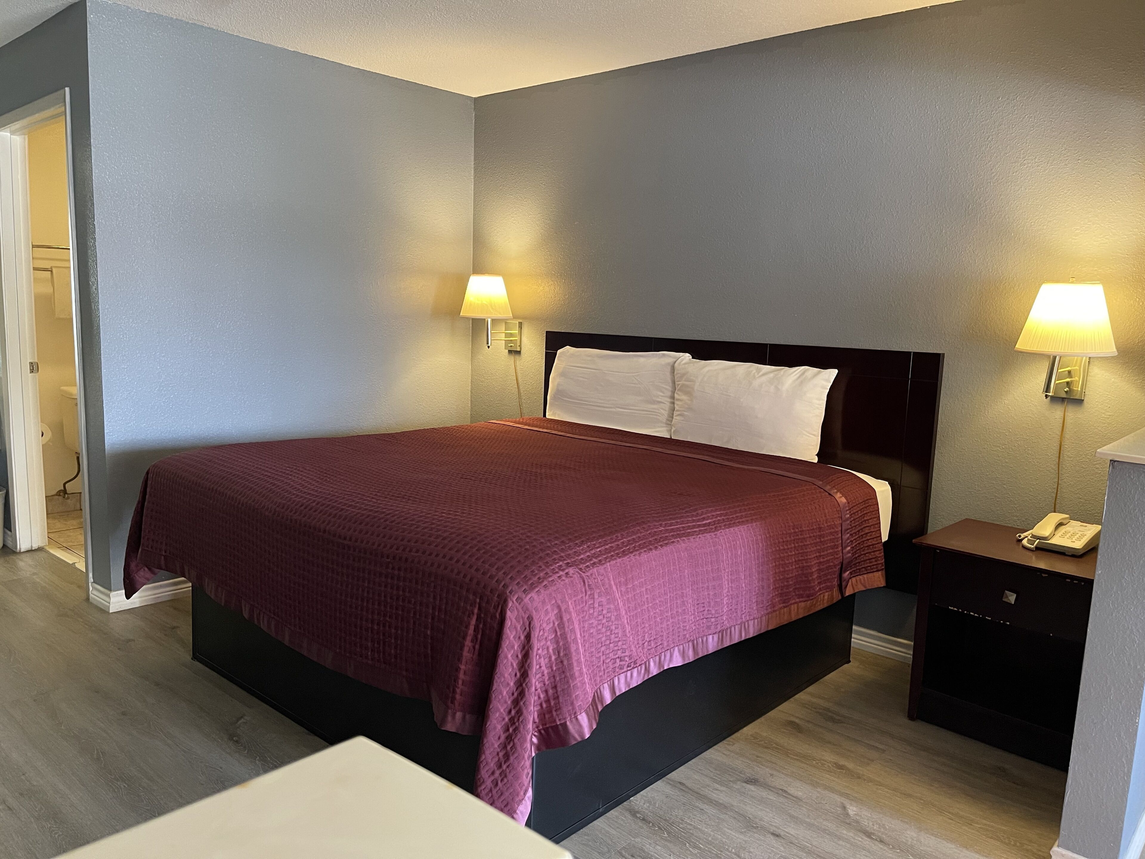 Una habitación de hotel con una cama grande, dos lámparas de noche, una mesita de noche con un teléfono y una puerta que da a un baño.