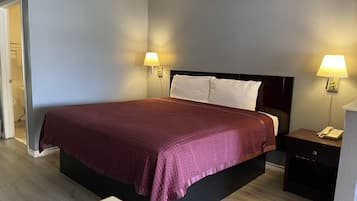 Una habitación de hotel con una cama grande, dos lámparas de noche, una mesita de noche con un teléfono y una puerta que da a un baño.