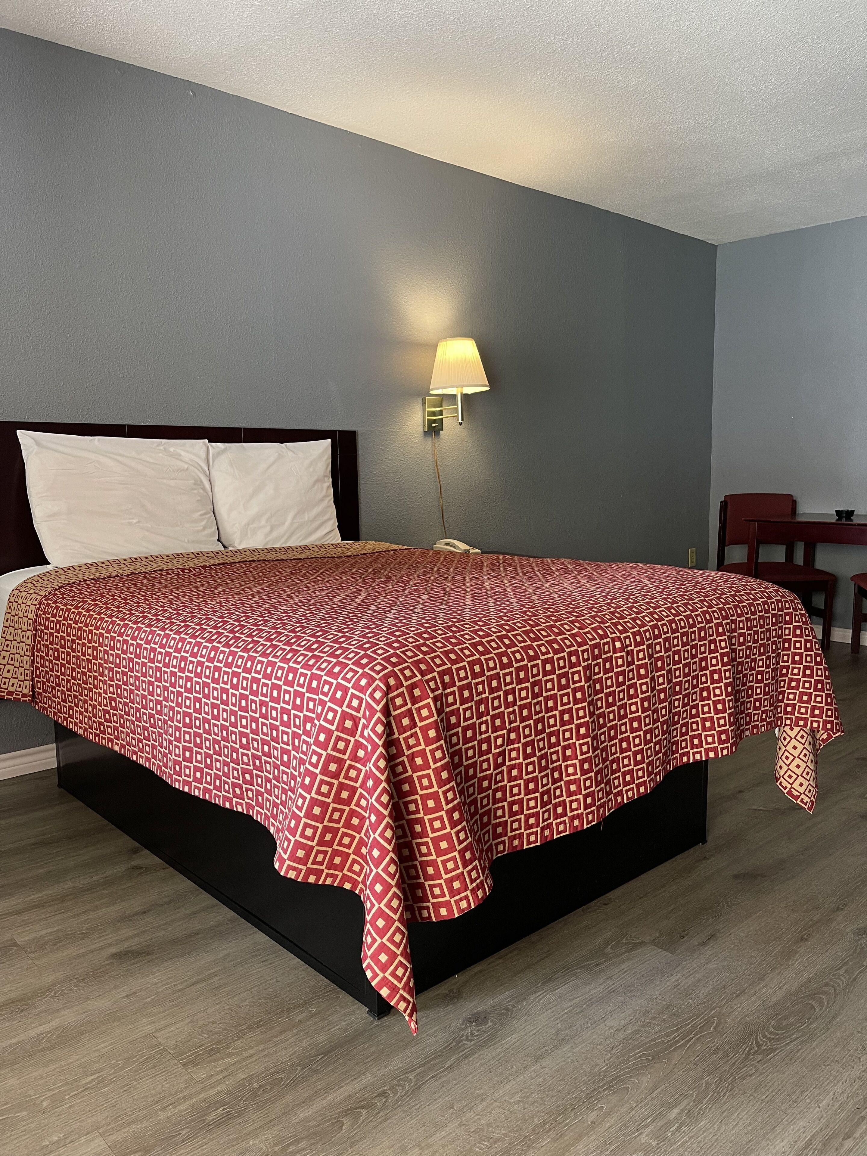 A neatly made bed with a patterned bedspread, a bedside lamp, and a wooden nightstand.