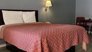 Una cama bien hecha con una colcha estampada, una lámpara de noche y una mesita de madera.