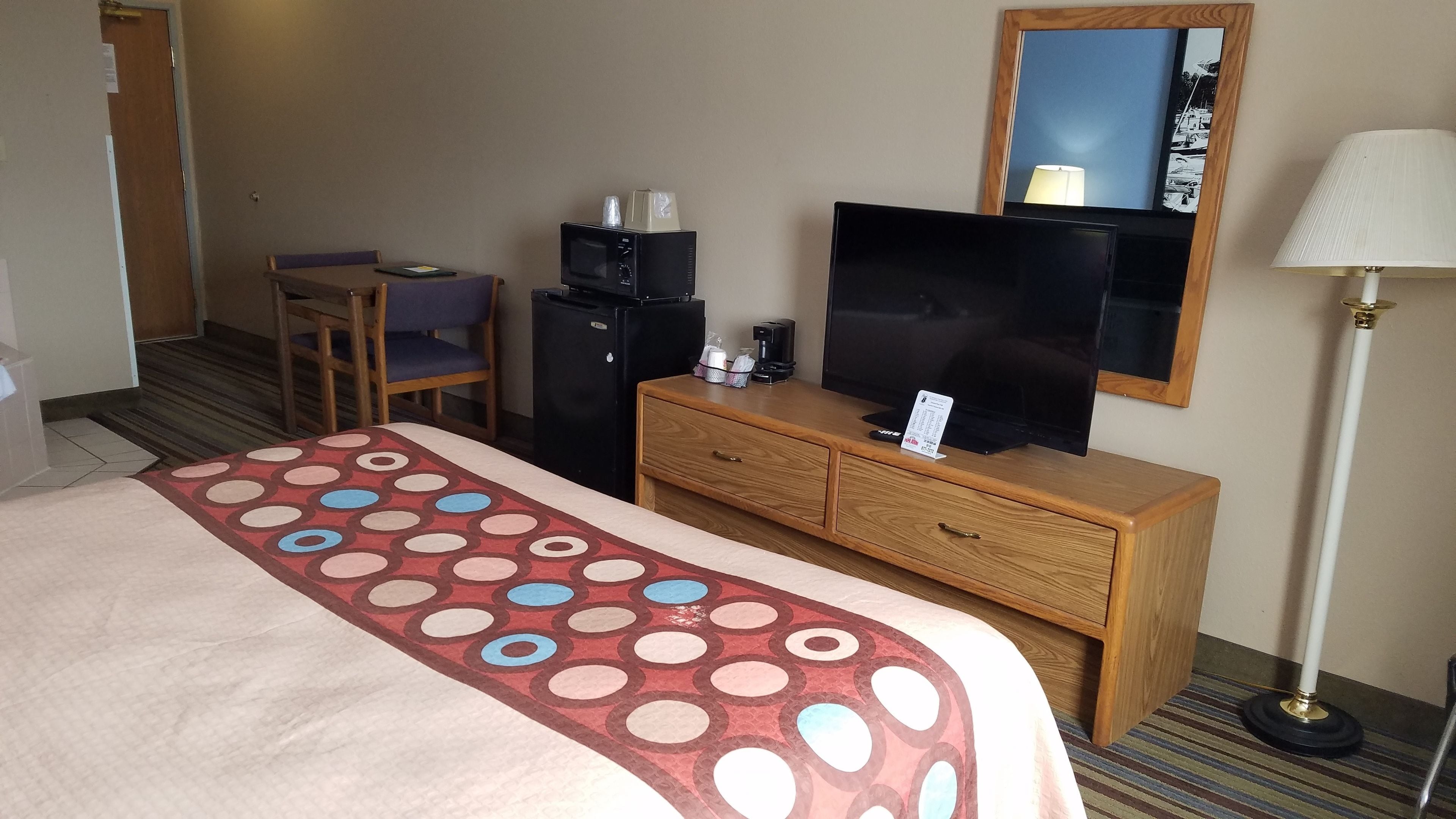 A hotel room with a bed, a desk with a computer, a television, a mirror, and a lamp.