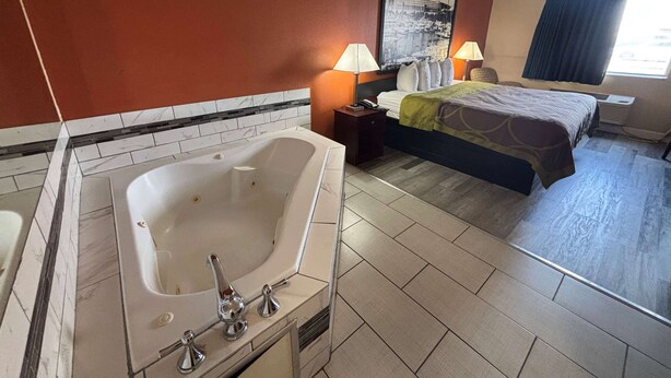 Une chambre d’hôtel avec une grande baignoire, un lit recouvert d’une couverture verte, deux lampes de chevet et une grande fenêtre donnant sur la ville.