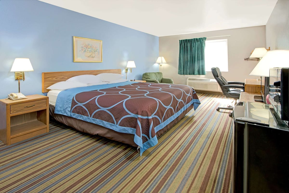 A hotel room with a bed, two bedside lamps, a desk with a computer, a chair, and a window with curtains.