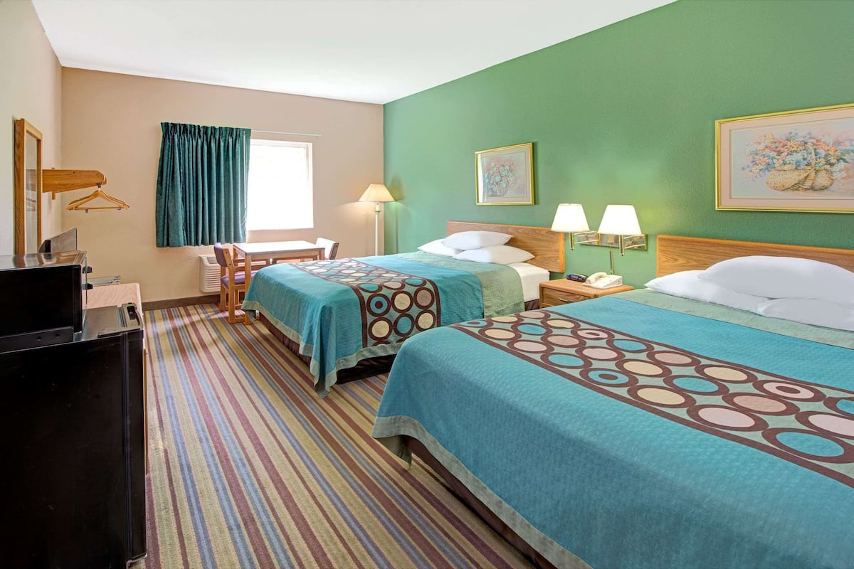 A hotel room with two beds, a desk, a chair, a TV, and a window with curtains.