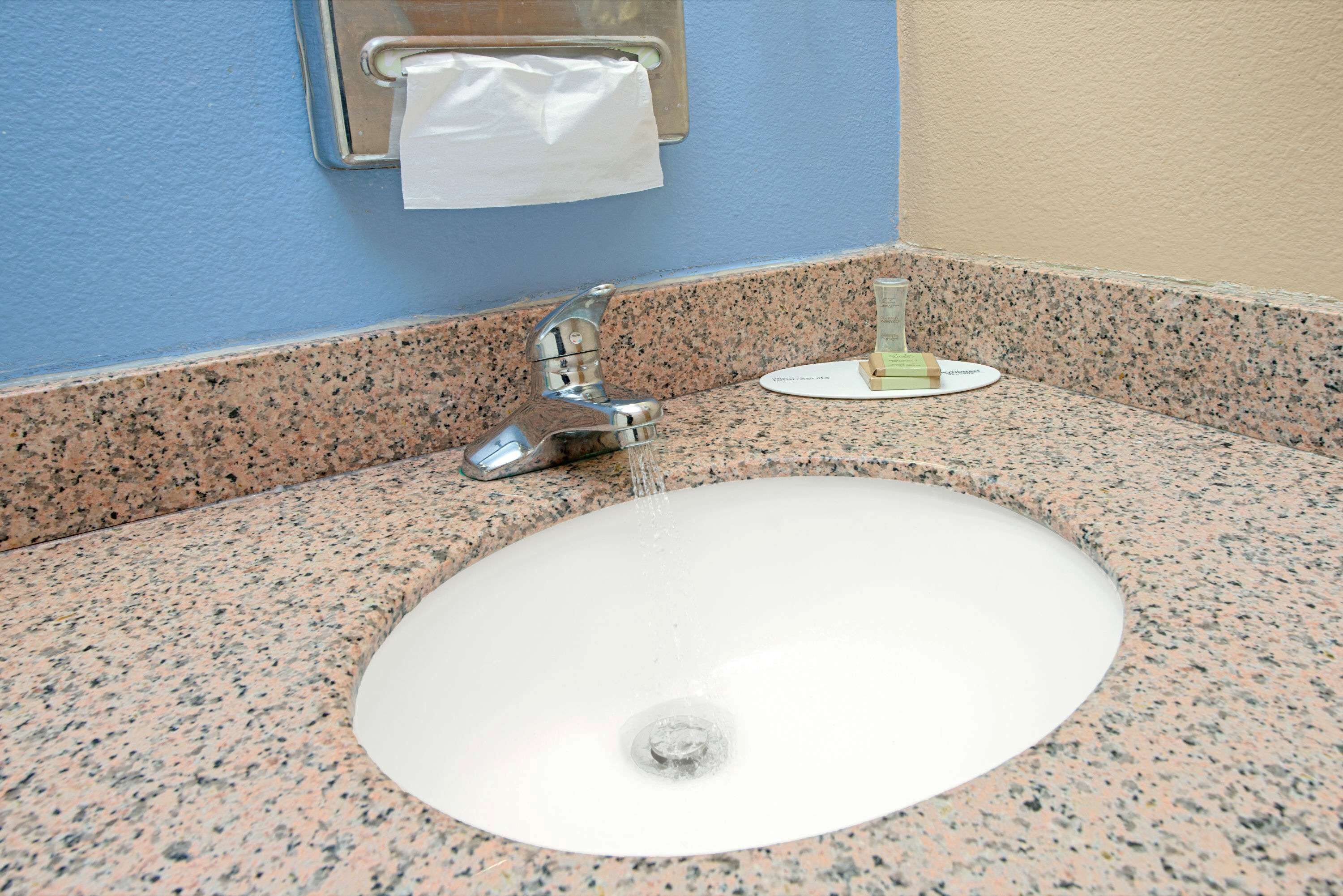 A bathroom sink with a granite countertop, a paper towel dispenser, and a soap dispenser.
