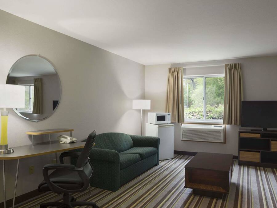 Een hotelkamer met een groene bank, een bureau met een lamp, een flatscreen televisie, een magnetron en een raam met gordijnen.